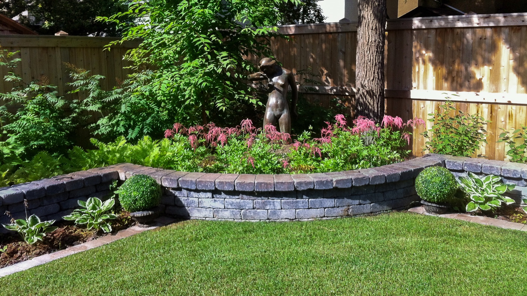 Clipped boxwood and perennials in a raised bed beside a manicured lawn