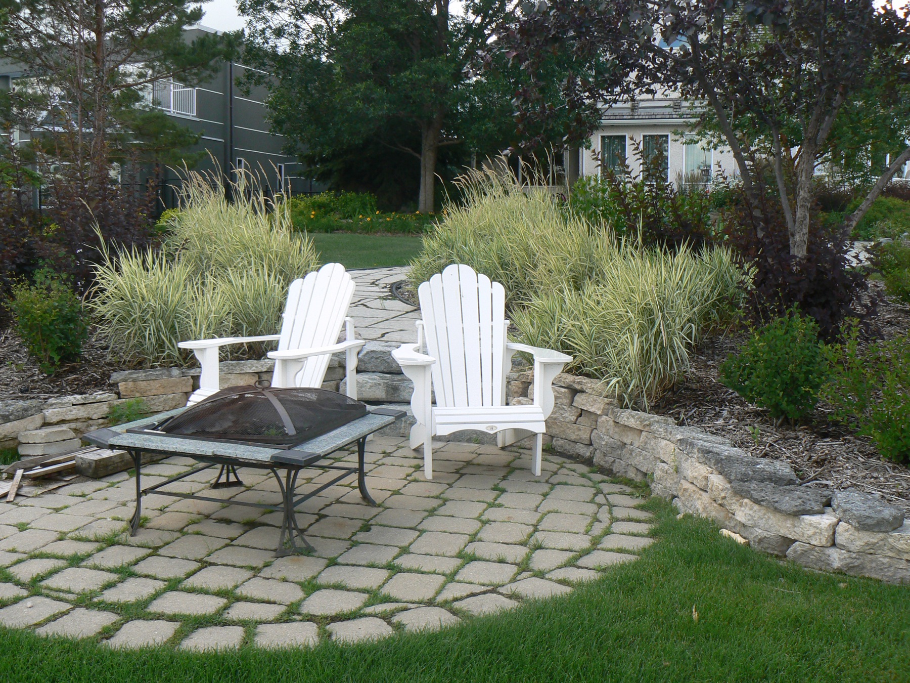 Fire pit patio with white Adirondack chairs under mature trees